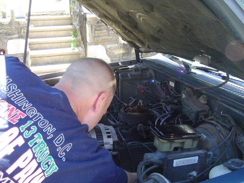 1993 Ford Bronco - A person works on the engine of a vehicle with the hood open.