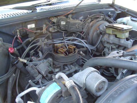 1993 Ford Bronco - A view of the engine bay, showing the carburetor, brake booster, and various hoses and wires.