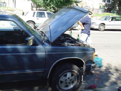 1993 Ford Bronco - A person works on the engine of a dark blue pickup truck parked on a street with other vehicles nearby.