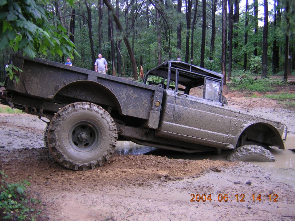 Mud-covered off-road vehicle stuck in mud, side view. Two people stand in background
