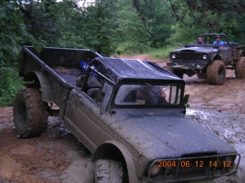 1984 Chevrolet Blazer - Two off-road vehicles navigate a muddy trail, kicking up dirt as they go.