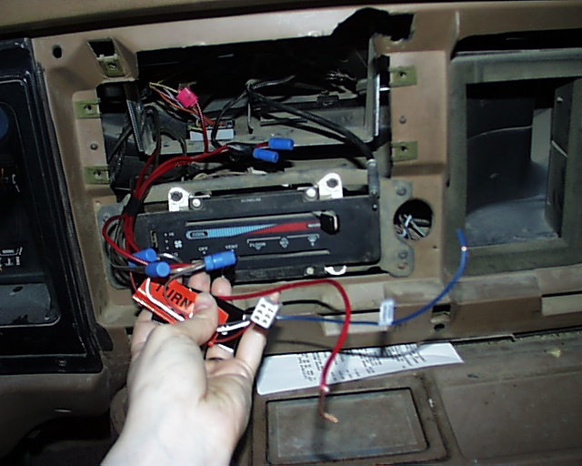 Hand holding aftermarket stereo wiring harness in an opened tan dash