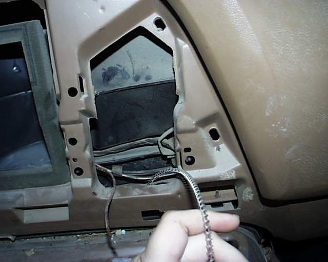 Hand routing speaker wire through opening in tan van dashboard