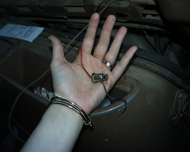 Hand holding small red and black two-wire electrical connector over brown engine bay