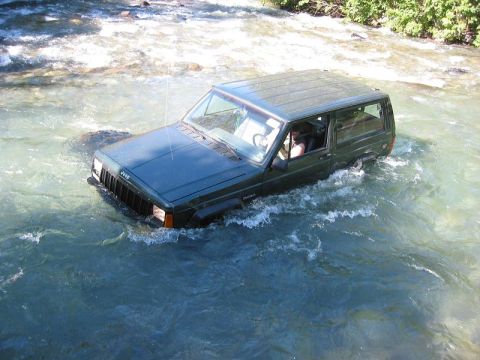 1985 Ford Bronco - A green Jeep Cherokee XJ navigates through a flowing river.