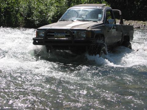 1985 Ford Bronco - This dark pickup truck navigates through a river, with its license plate EKC 534 clearly visible.