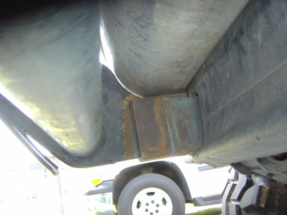 Underside of a vehicle showing rusted metal brackets and a tire