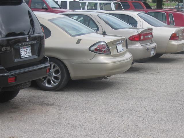 Gold sedan, black SUV, and red SUV parked in a lot. The sedan has a spoiler and distinctive taillights