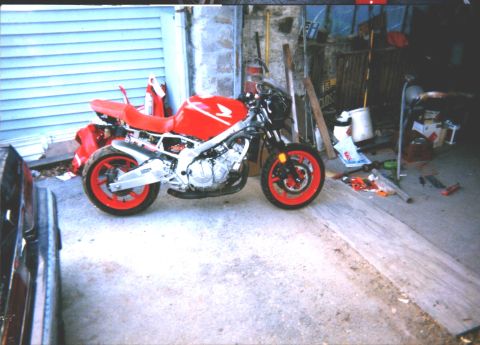 1994 Ford Bronco - A red motorcycle with red wheels is parked in a cluttered garage.