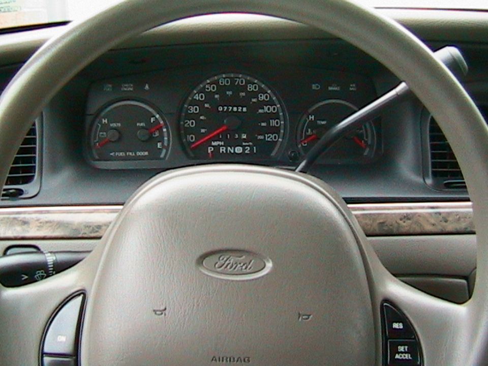 Ford gauge cluster through tan steering wheel showing 77,828 miles and 120 mph speedometer