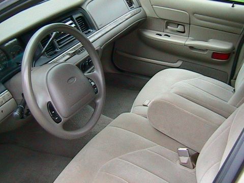 2000 Ford Crown Victoria - The interior of a 2000 Ford Crown Victoria features tan cloth seats, a tan dashboard, and a tan steering wheel.