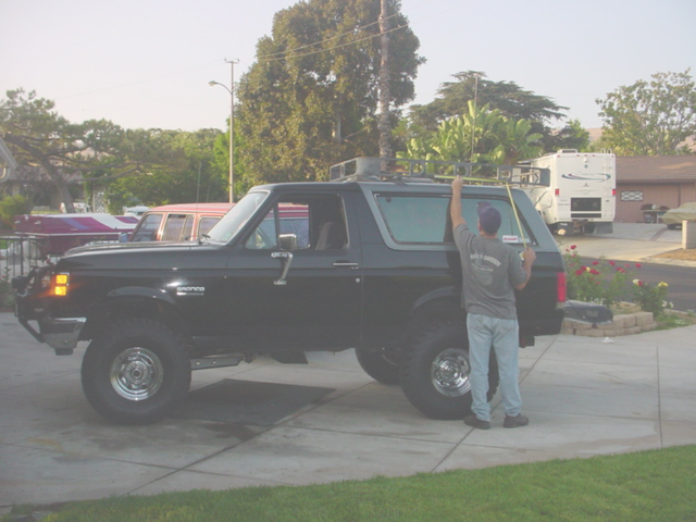 Black lifted Ford Bronco full-size 4x4 SUV in driveway with man reaching for roof rack