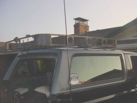 1988 Ford Bronco - A custom roof rack is mounted on the top of an SUV, with a brick chimney visible in the background.