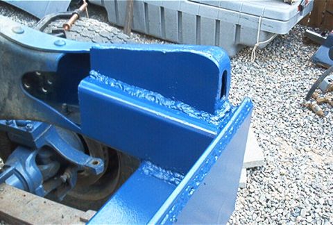 1986 Ford Bronco - Close-up of a freshly blue-painted, heavily welded steel bracket or mount fabricated onto a vehicle frame, with a cast component and drivel…