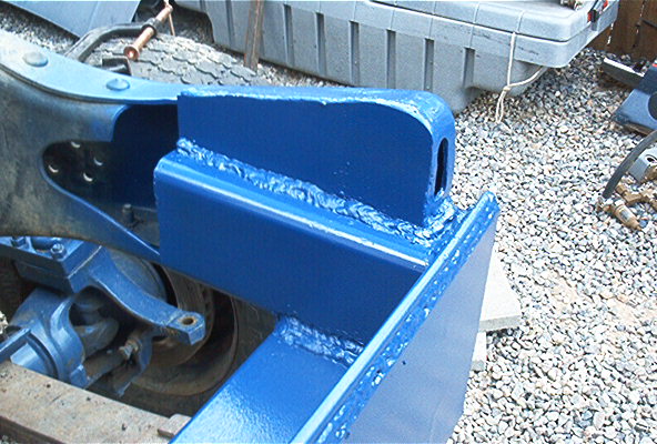 Blue-painted welded steel frame bracket with visible weld beads, outdoors on gravel