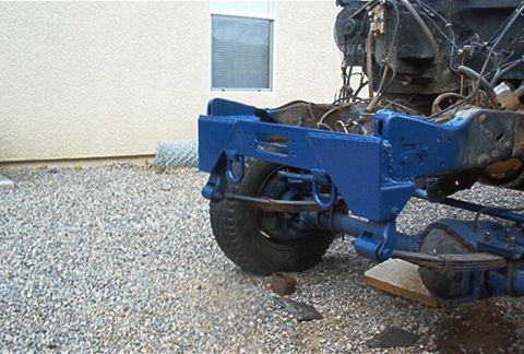 1986 Ford Bronco - Close-up of a freshly painted blue steel frame section and rear leaf-spring suspension on a partially disassembled truck chassis, with a ba…