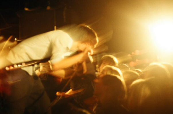 Musician playing guitar on stage with bright lights and crowd