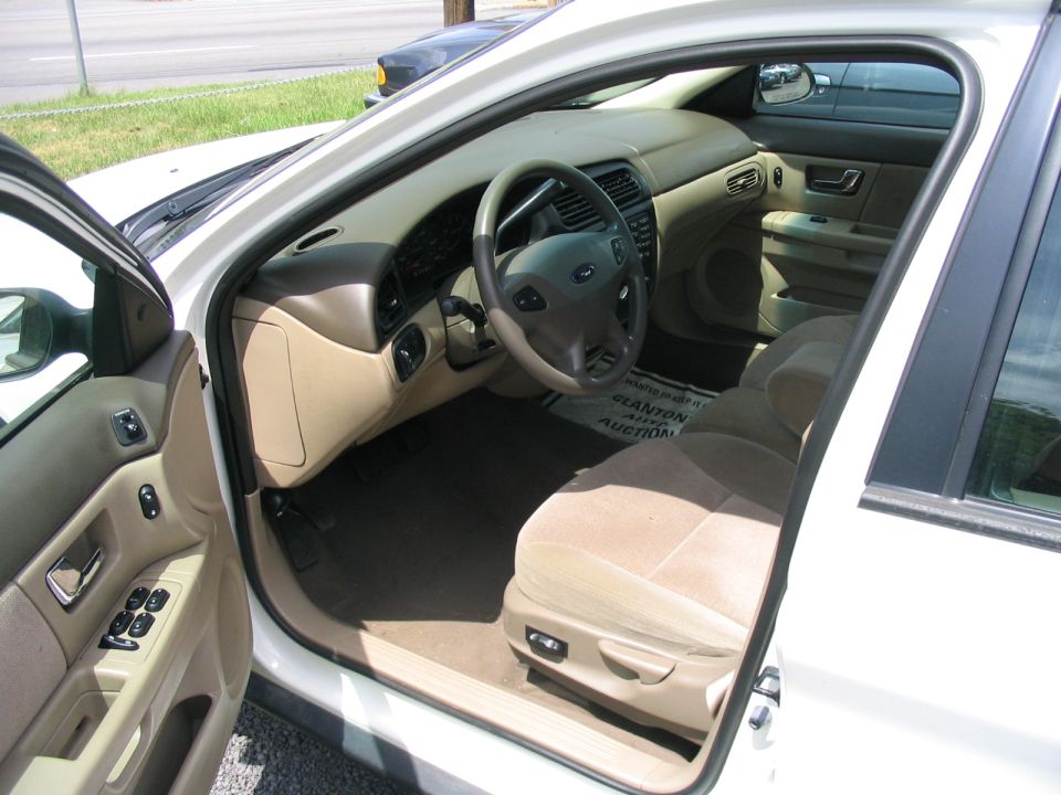 Tan interior of white Ford sedan through open driver door with Ford steering wheel