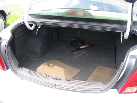 2000 Honda Accord - The trunk of a white sedan is shown, revealing the spare tire and jack, along with two floor mats.