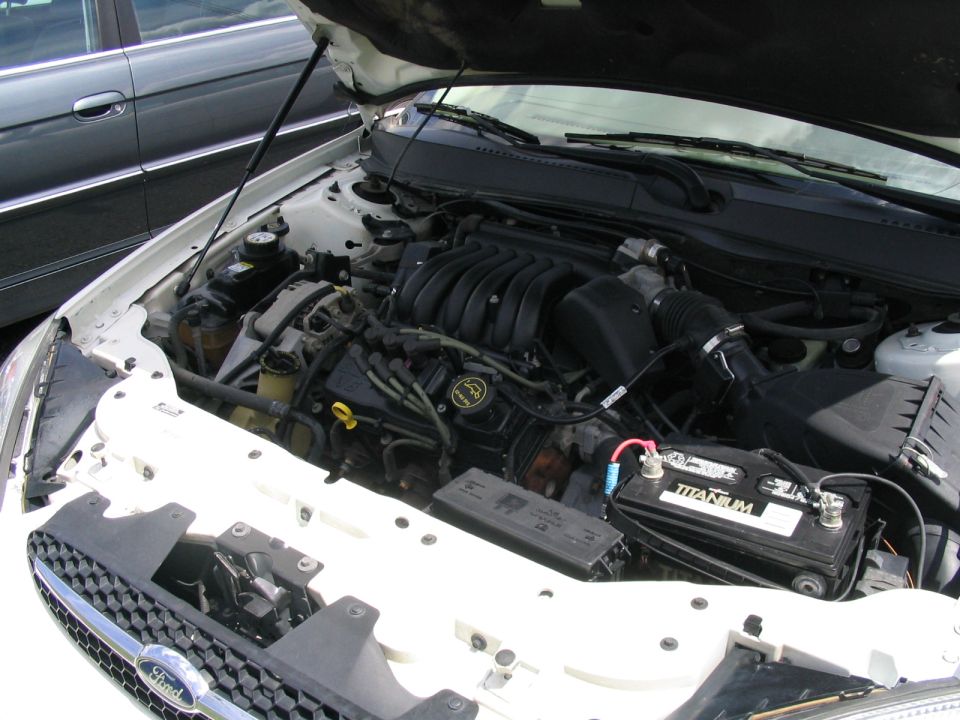 White Ford sedan engine bay with black V6 intake manifold and Titanium battery