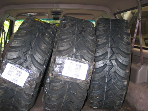 1995 Ford Bronco - Three large off-road tires are packed in the cargo area of a vehicle.