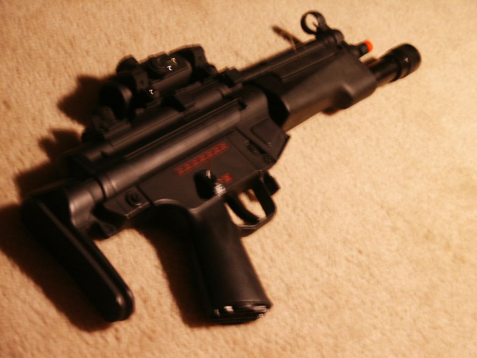 Black submachine gun with red markings and optic sight