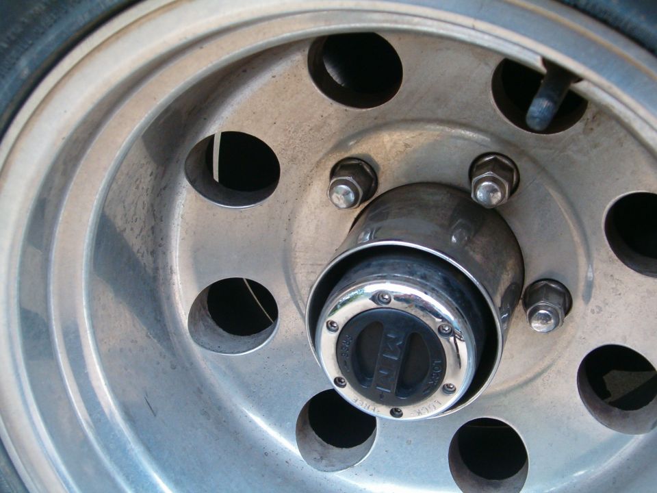 Close-up of a vehicle's wheel hub with lug nuts and a black and chrome locking mechanism