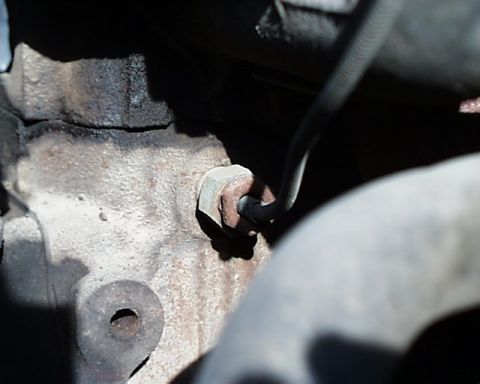 1988 Ford E250 - A close-up view of a bolt and a hose attached to a heavily soiled engine component.