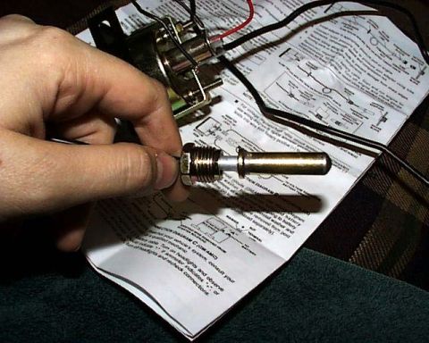1988 Ford E250 - A hand holds a brass sensor over a folded wiring diagram with electrical components and wires visible.