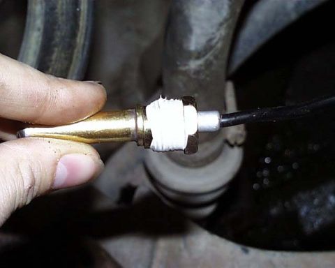 1988 Ford E250 - Close-up of a hand installing a brass automotive component with tape and a cable attached.
