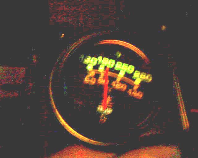 Illuminated round vehicle gauge at night with red needle and green and amber scales