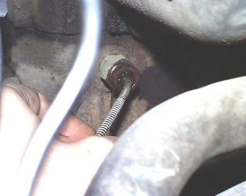 1988 Ford E250 - A hand manipulates a cable attached to an engine part, surrounded by hoses and engine block components.