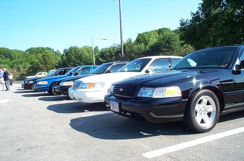 2001 Ford Crown Victoria - Multiple Ford Crown Victoria police cars are lined up in a parking lot under a clear blue sky.