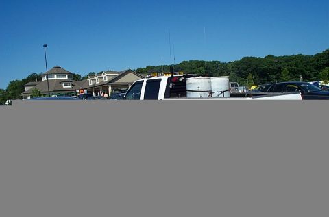 2001 Ford Crown Victoria - A white truck with two large cylindrical tanks in its bed is parked in a lot near a building.