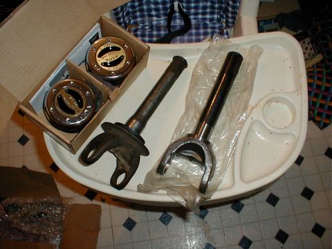1983 Ford Bronco - A pair of Warn locking hubs still in their box sits beside two front axle shafts with U-joint yokes, one used and one new in plastic wrap,…