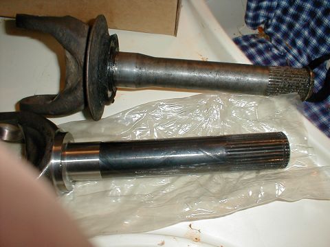 1983 Ford Bronco - Two axle shafts with U-joint yokes laid side by side on a white surface for comparison, the used one at top still has its slinger and oil-s…