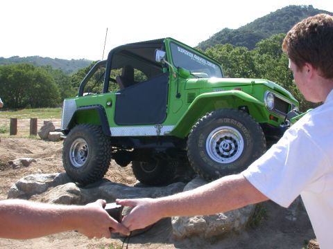 1996 Ford Bronco - A green off-road vehicle navigates a rocky terrain with two people in the foreground.