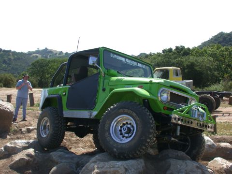 1996 Ford Bronco - A green off-road vehicle navigates a rocky terrain, with a yellow truck visible in the background.