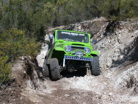 1996 Ford Bronco - A bright green off-road vehicle tackles a challenging, rocky incline on a sunny day.
