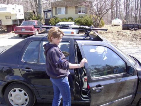 1994 Ford Bronco - A person opens the door of a black sedan equipped with a roof rack, with another vehicle and a trailer visible in the background.