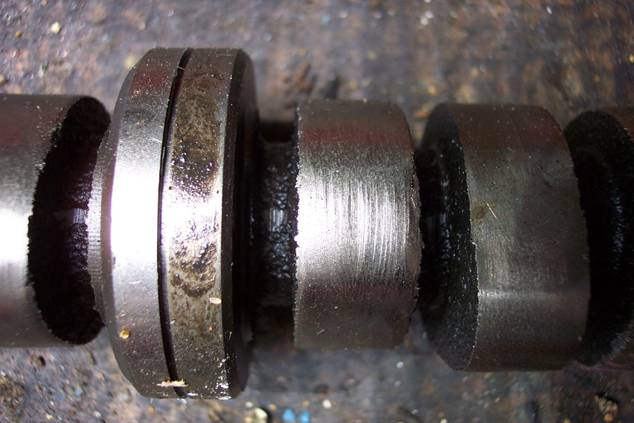 Close-up of an engine camshaft lobe and journal showing wear scoring and oil residue