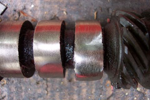 1968 Ford F-100 - Extreme close-up of an engine camshaft laid on a concrete floor, showing three polished bearing journals and dark oiled lobes with traces o…
