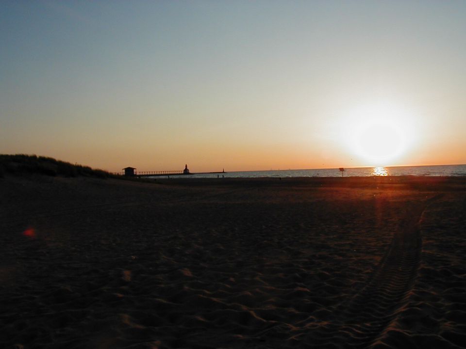 Beach dunes and pier at sunset with tire tracks in the sand