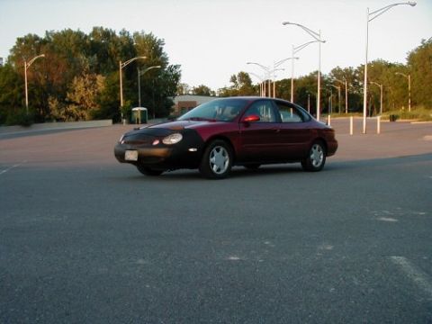 1997 Ford Taurus - A red 1997 Ford Taurus sedan is parked in an empty lot, equipped with a car bra on its front end.