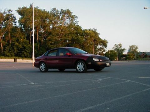 1997 Ford Taurus - A maroon sedan sits in a large, empty parking lot under a clear sky.