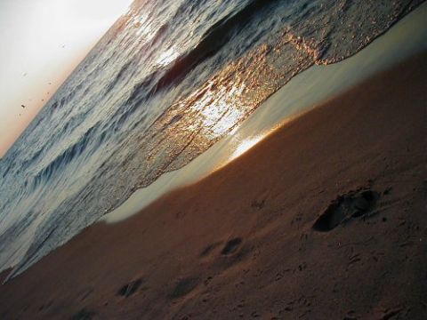 1997 Ford Taurus - A tranquil beach scene at sunset with gentle waves lapping the shore and footprints in the sand.