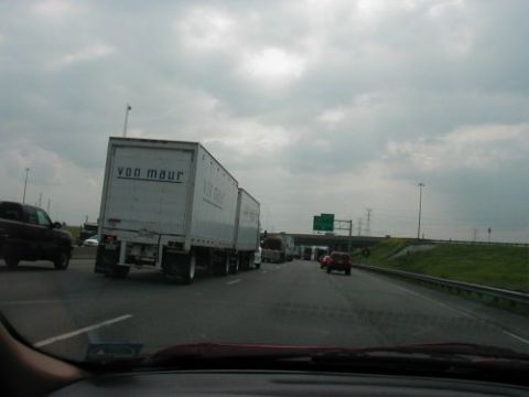 1997 Ford Taurus - Traffic jam on the highway with multiple trucks and cars. "von maur" text on trailer.
