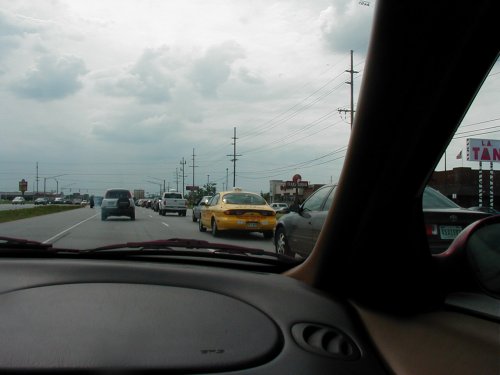 Driving in traffic on a cloudy day, yellow taxi ahead, other cars in lanes