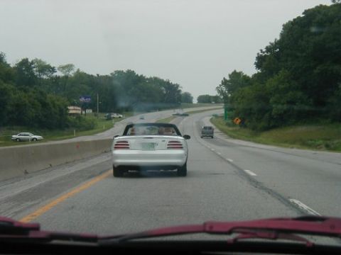 1997 Ford Taurus - A white convertible sports car is seen from behind on a highway, emitting smoke.
