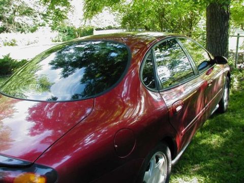 1997 Ford Taurus - Rear quarter view of a red 1997 Ford Taurus sedan parked on a grassy lawn.